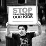 black and white image of young boy with brows furrowed and mouth open, holding a sign which says "STOP BRAINWASHING OUR KIDS"