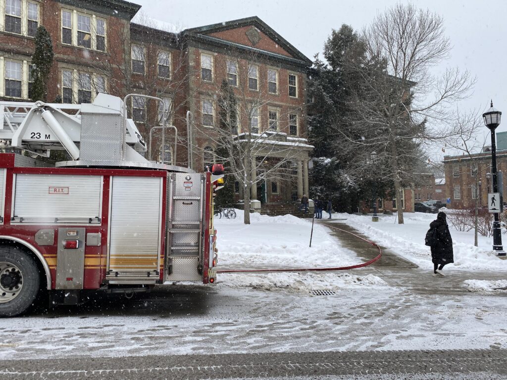 fire truck in front of old forestry building while it's snowing, a person dressed in black is at walking in the far right of the image