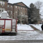 fire truck in front of old forestry building while it's snowing, a person dressed in black is at walking in the far right of the image