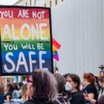 Image of sign above crowd saying "YOU ARE NOT ALONE YOU WILL BE SAFE"