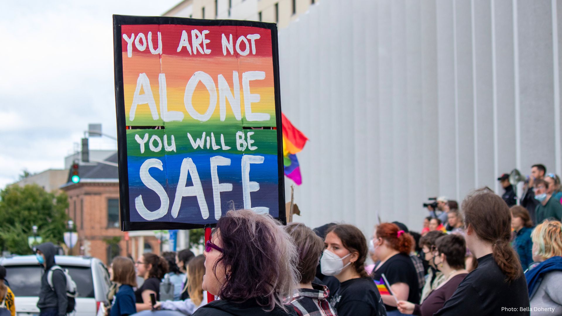 Image of sign above crowd saying "YOU ARE NOT ALONE YOU WILL BE SAFE"
